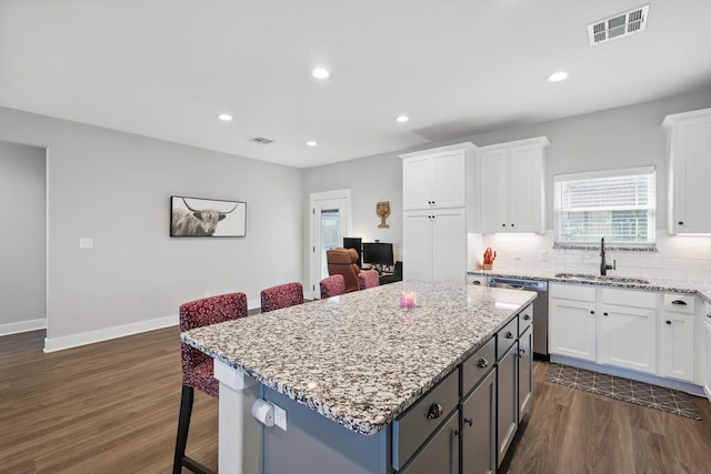 kitchen featuring visible vents, white cabinets, dishwasher, a kitchen bar, and a sink