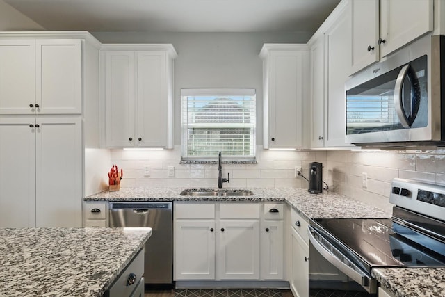 kitchen featuring tasteful backsplash, white cabinets, appliances with stainless steel finishes, light stone countertops, and a sink