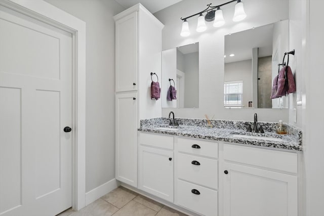 bathroom with baseboards, double vanity, a sink, and tile patterned floors