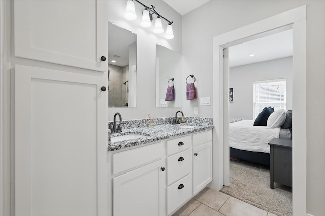 ensuite bathroom with a tile shower, double vanity, tile patterned flooring, and a sink