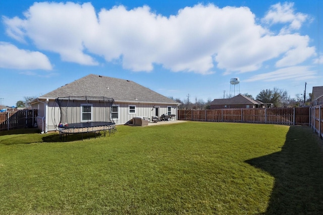 rear view of property with a trampoline, a yard, board and batten siding, a patio area, and a fenced backyard