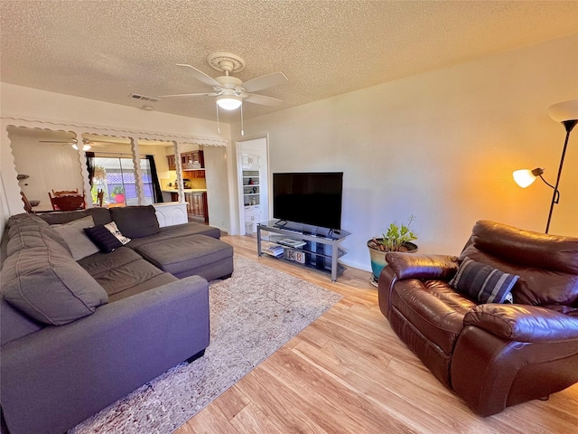 living room with light wood-style floors, visible vents, ceiling fan, and a textured ceiling