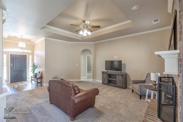 carpeted living room with arched walkways, crown molding, a raised ceiling, visible vents, and baseboards