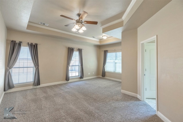 carpeted empty room with visible vents, baseboards, ceiling fan, ornamental molding, and a tray ceiling