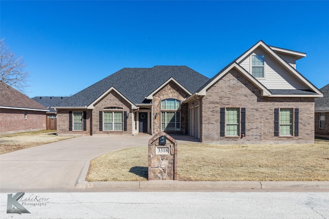 view of front of property featuring a front yard, brick siding, driveway, and roof with shingles