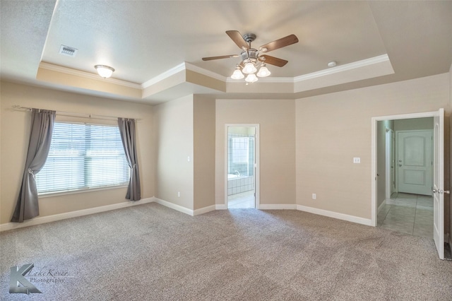 carpeted empty room with a tray ceiling, visible vents, crown molding, and baseboards