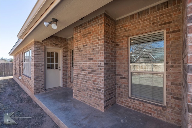 view of exterior entry featuring brick siding and fence