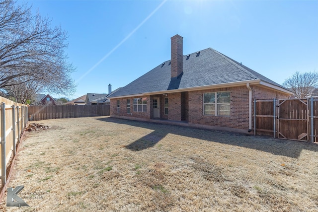 rear view of house with a fenced backyard, brick siding, a yard, a gate, and a chimney