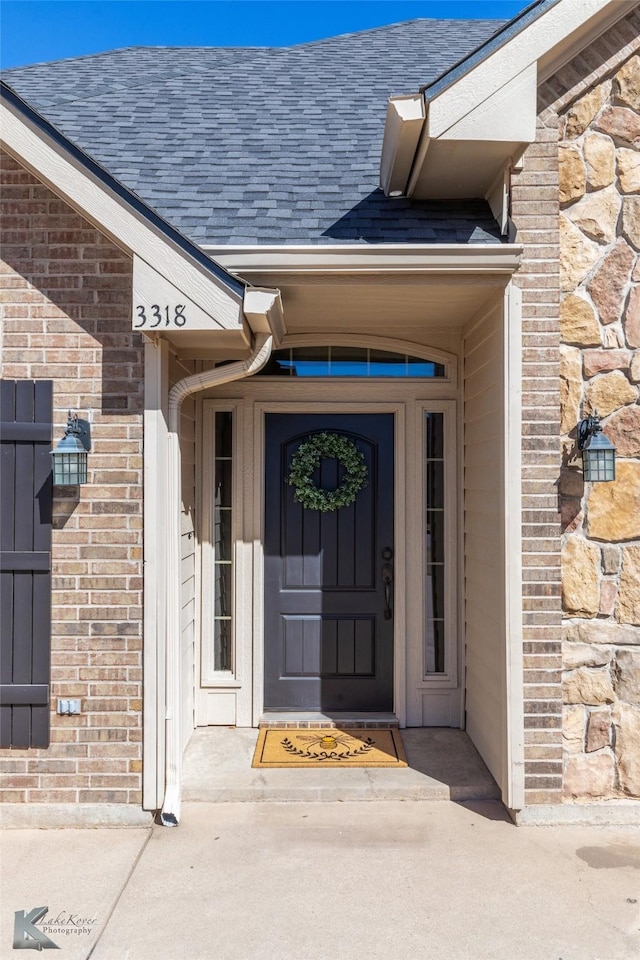 property entrance with a shingled roof, stone siding, and brick siding