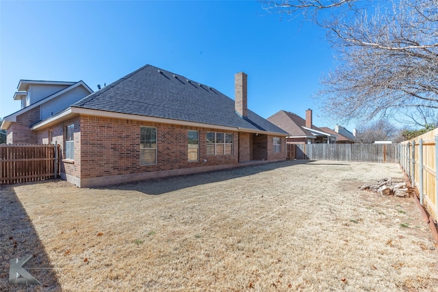 rear view of house featuring a fenced backyard, brick siding, roof with shingles, a lawn, and a chimney