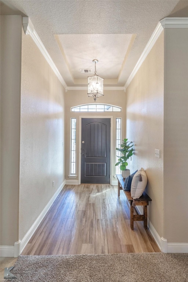 foyer featuring a textured ceiling, wood finished floors, visible vents, and crown molding