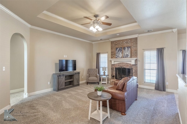 carpeted living room with a fireplace, a raised ceiling, visible vents, and crown molding