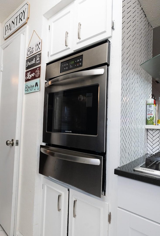 kitchen featuring oven, white cabinetry, decorative backsplash, a warming drawer, and dark countertops