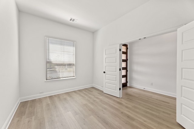 empty room featuring light wood-style floors, visible vents, and baseboards