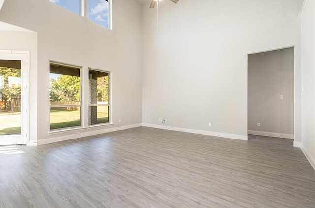 empty room featuring a high ceiling, a healthy amount of sunlight, baseboards, and wood finished floors