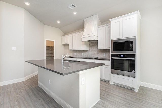 kitchen featuring visible vents, dark countertops, premium range hood, stainless steel oven, and a sink