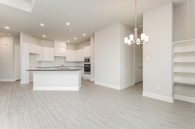 kitchen with wall oven, light wood-style flooring, open floor plan, dark countertops, and custom range hood