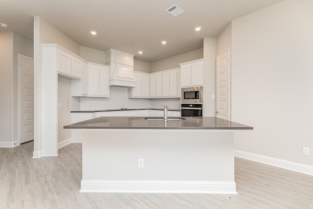 kitchen with appliances with stainless steel finishes, dark countertops, custom range hood, and white cabinetry