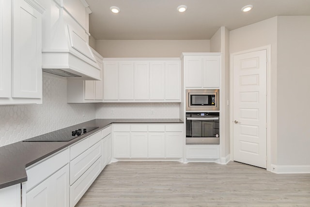 kitchen featuring light wood finished floors, appliances with stainless steel finishes, white cabinets, and custom range hood