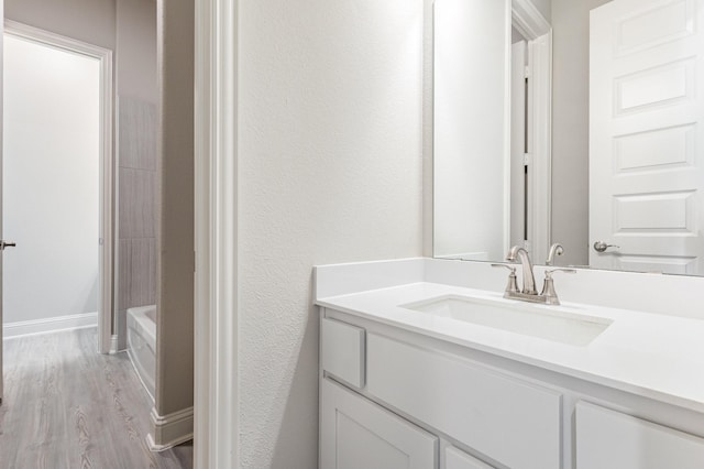 full bath featuring a tub, baseboards, wood finished floors, and vanity