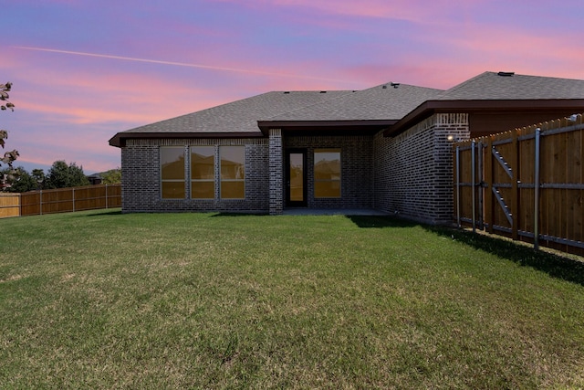 rear view of property featuring a yard, a fenced backyard, roof with shingles, and brick siding