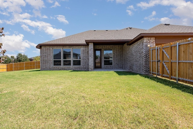 rear view of house with brick siding, a lawn, a fenced backyard, and roof with shingles