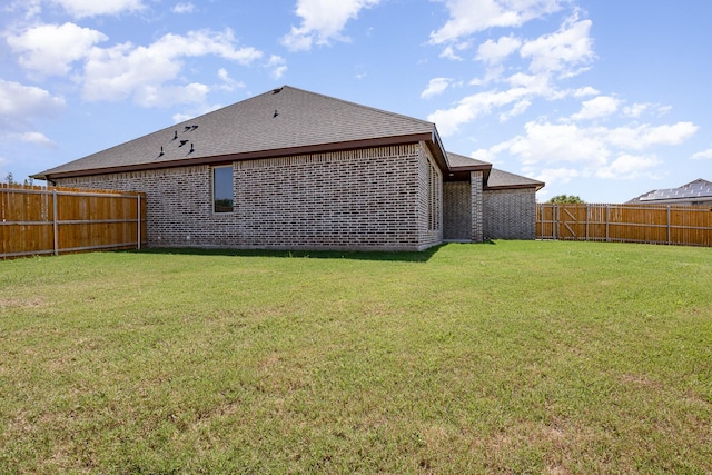 back of house with a fenced backyard, roof with shingles, a lawn, and brick siding