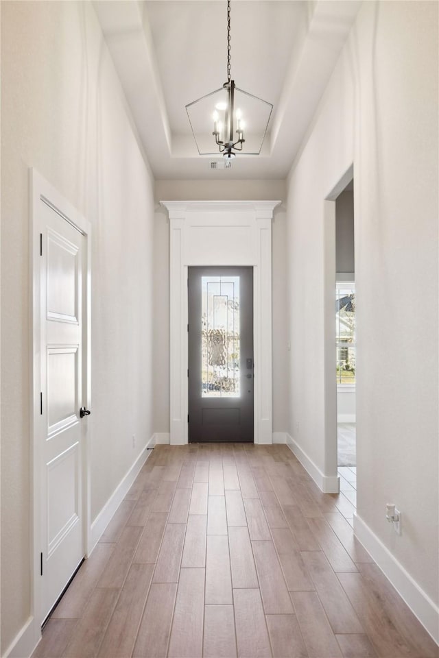 entryway featuring a chandelier, a tray ceiling, wood finish floors, and baseboards