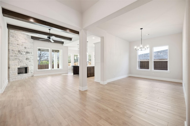 unfurnished living room with ceiling fan with notable chandelier, a fireplace, baseboards, light wood-style floors, and beam ceiling