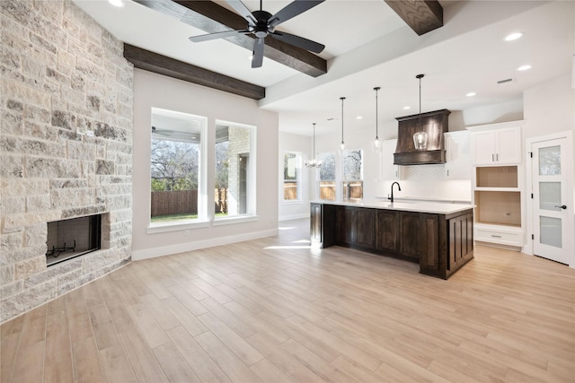 kitchen with a stone fireplace, light wood-style flooring, premium range hood, light countertops, and beamed ceiling