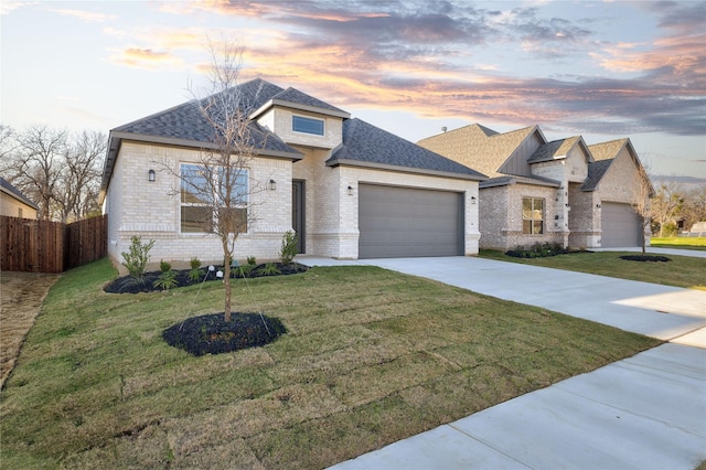 french country inspired facade with concrete driveway, a front lawn, an attached garage, and fence