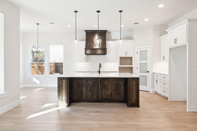 kitchen featuring a spacious island, tasteful backsplash, custom range hood, and light wood-style flooring