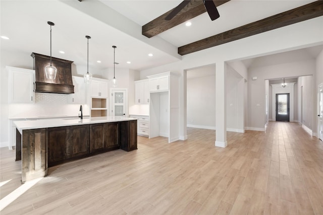 kitchen featuring light wood finished floors, light countertops, beam ceiling, and a large island with sink