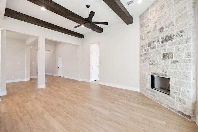 unfurnished living room featuring light wood-style flooring, a ceiling fan, a stone fireplace, beamed ceiling, and baseboards