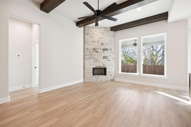 unfurnished living room featuring beam ceiling, light wood-style floors, a ceiling fan, a stone fireplace, and baseboards