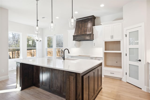 kitchen featuring black electric stovetop, custom exhaust hood, decorative backsplash, a sink, and light wood-type flooring