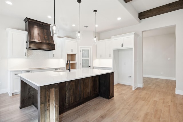 kitchen featuring custom exhaust hood, light wood-style flooring, white cabinetry, a sink, and a large island with sink