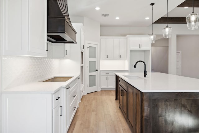 kitchen featuring black electric stovetop, light wood finished floors, custom range hood, visible vents, and a sink