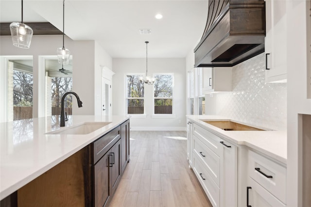 kitchen featuring tasteful backsplash, visible vents, custom range hood, black electric stovetop, and a sink