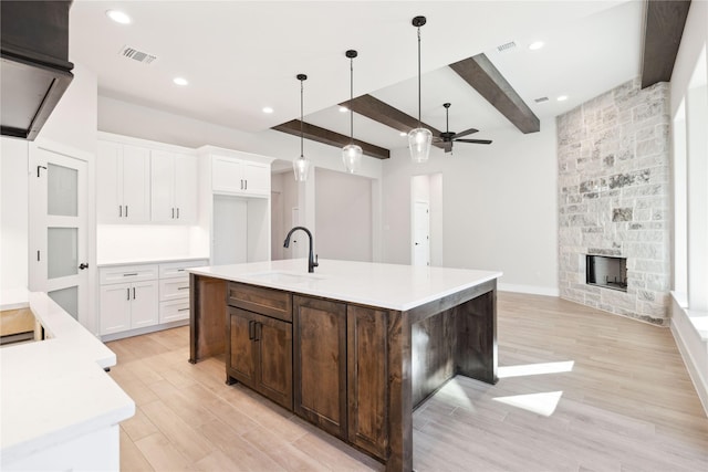 kitchen with visible vents, a sink, a stone fireplace, white cabinetry, and beam ceiling