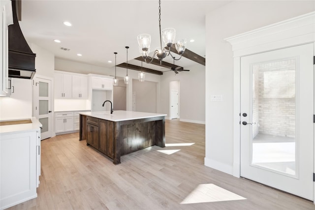 kitchen with light countertops, light wood-type flooring, premium range hood, and an island with sink