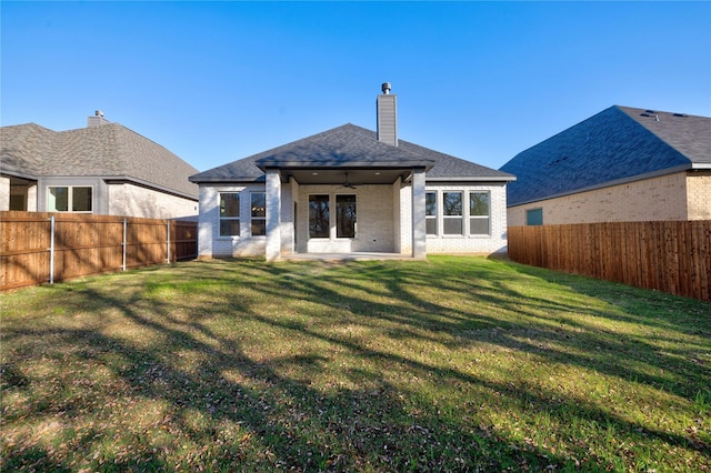 rear view of house featuring brick siding, a fenced backyard, a chimney, and a yard