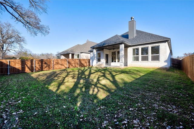 back of house with brick siding, a fenced backyard, a chimney, and a yard