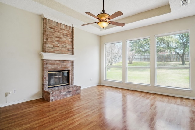 unfurnished living room with a fireplace, wood finished floors, visible vents, and a healthy amount of sunlight