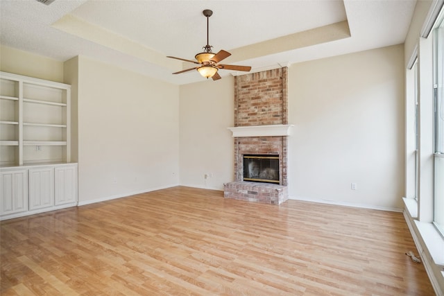 unfurnished living room featuring baseboards, ceiling fan, a tray ceiling, light wood-style floors, and a fireplace