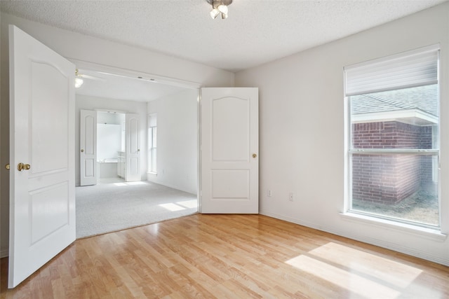 empty room featuring light wood-style floors, a textured ceiling, and baseboards