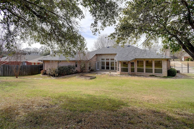 back of property featuring a sunroom, fence, a lawn, and brick siding