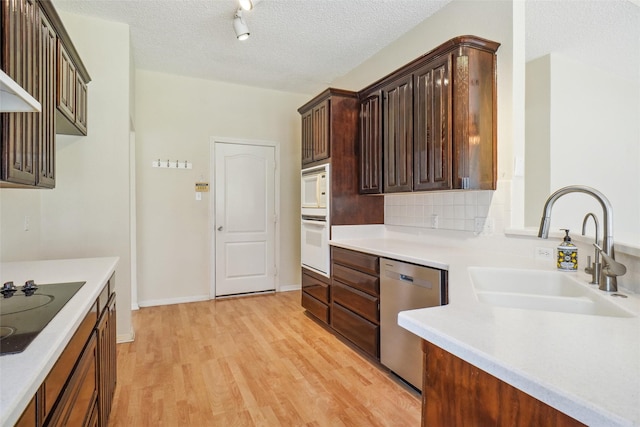 kitchen with a textured ceiling, light wood-style flooring, white appliances, a sink, and decorative backsplash