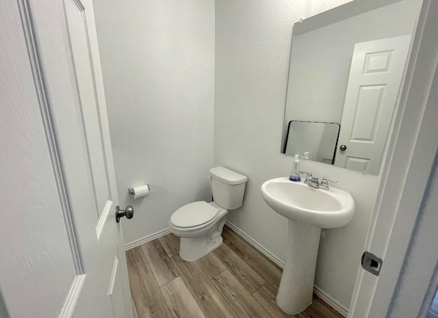 half bath with a sink, wood finished floors, toilet, and baseboards