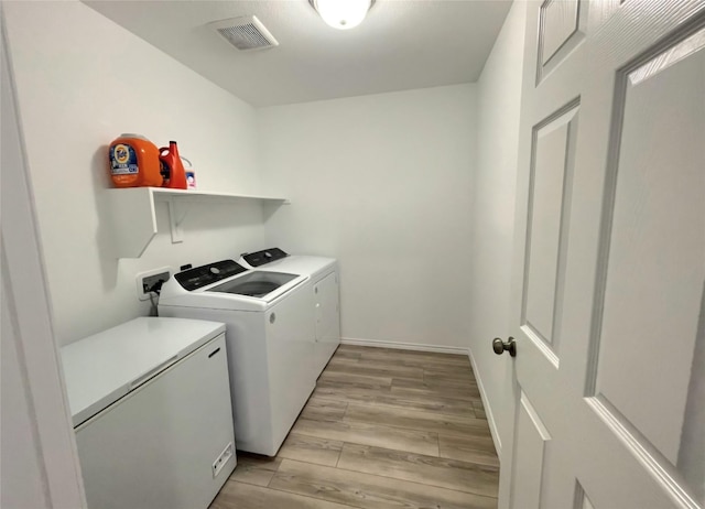 laundry room with washing machine and clothes dryer, visible vents, light wood-style floors, laundry area, and baseboards